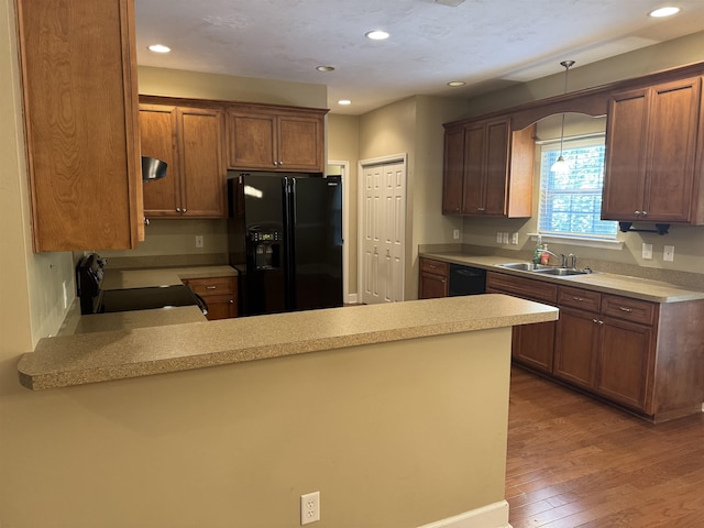 kitchen with hanging light fixtures, a sink, light countertops, a peninsula, and black appliances