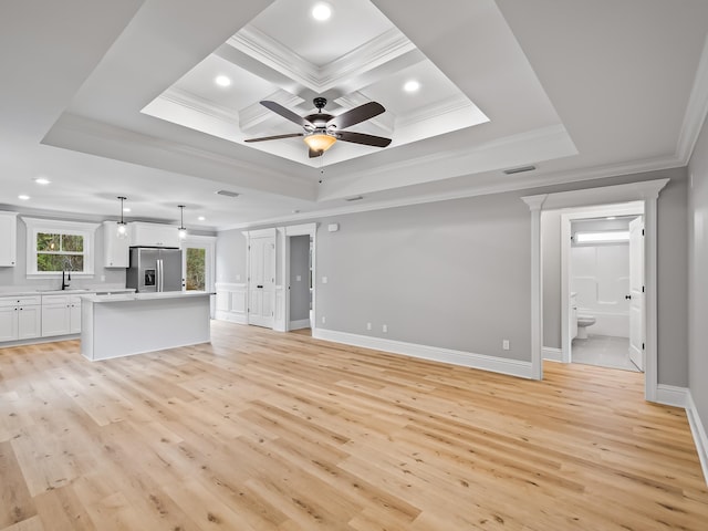 unfurnished living room featuring a raised ceiling, ceiling fan, crown molding, sink, and light hardwood / wood-style floors