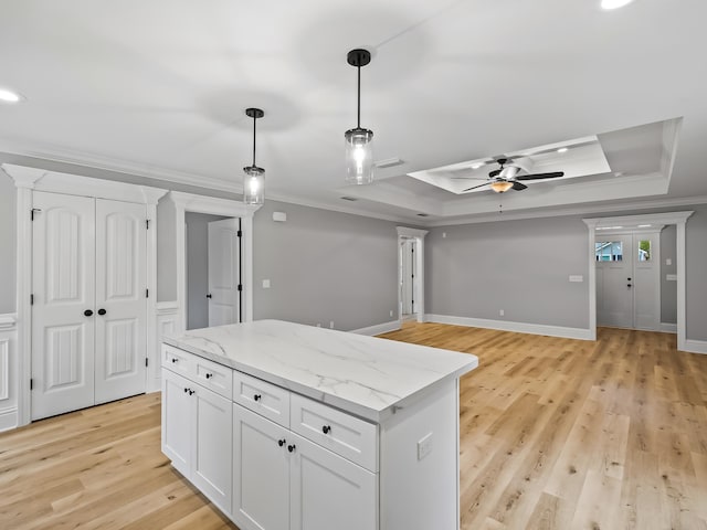 kitchen featuring white cabinets, light hardwood / wood-style floors, a raised ceiling, and ornamental molding