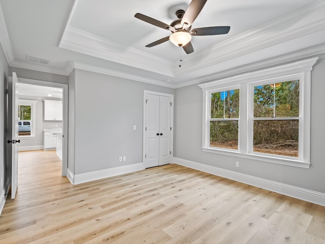 unfurnished bedroom featuring light hardwood / wood-style floors, ceiling fan, ornamental molding, and a tray ceiling