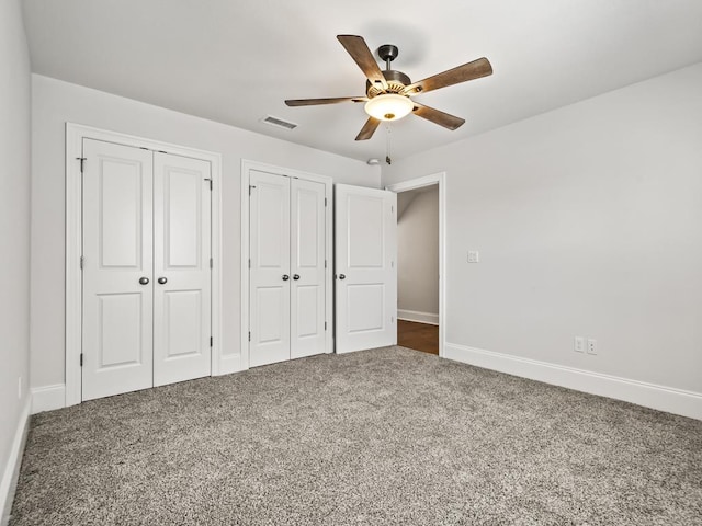 unfurnished bedroom featuring two closets, dark carpet, and ceiling fan