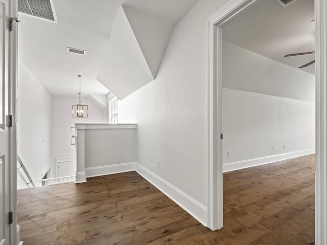 hallway featuring a notable chandelier, dark wood-type flooring, and vaulted ceiling