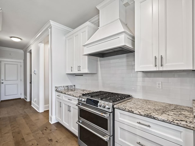 kitchen featuring backsplash, light stone counters, custom exhaust hood, double oven range, and white cabinets