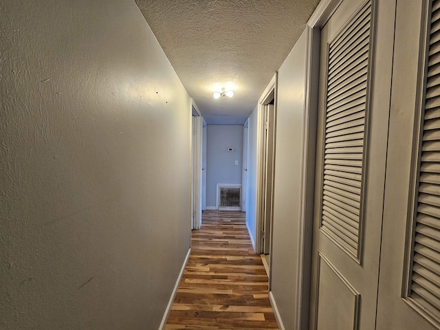 corridor with a textured ceiling and dark wood-type flooring