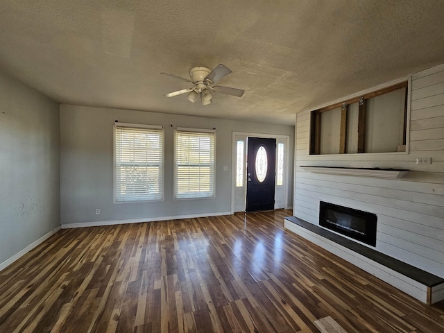 foyer entrance with a fireplace, ceiling fan, dark wood-type flooring, and a textured ceiling