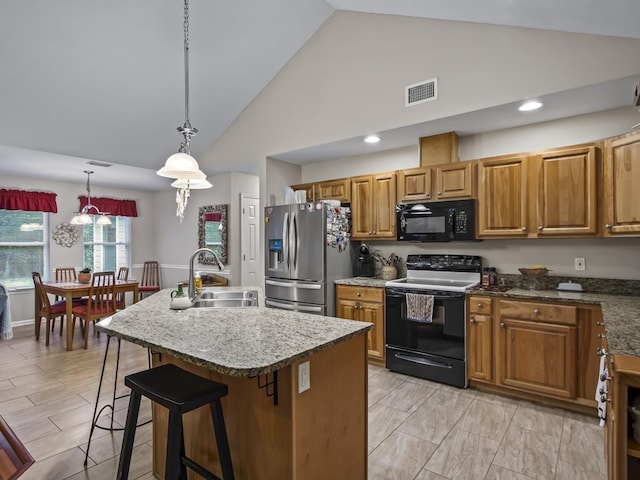 kitchen with pendant lighting, a kitchen island with sink, black appliances, sink, and a breakfast bar area