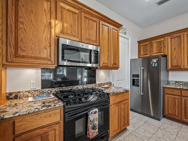 kitchen with backsplash, light tile patterned floors, light stone countertops, and appliances with stainless steel finishes