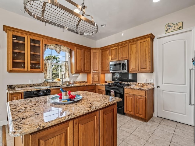 kitchen featuring pendant lighting, sink, a center island, light stone counters, and black appliances