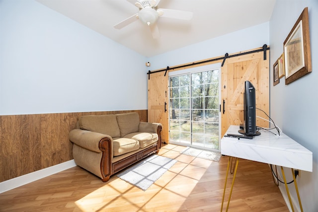 23380 Elmwood Ln, Live Oak, FL 32064 - sitting room featuring a barn door, light wood-style floors, wainscoting, ceiling fan, and wooden walls