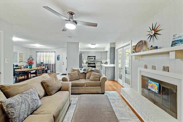 living room with a brick fireplace, light hardwood / wood-style floors, a textured ceiling, and ceiling fan