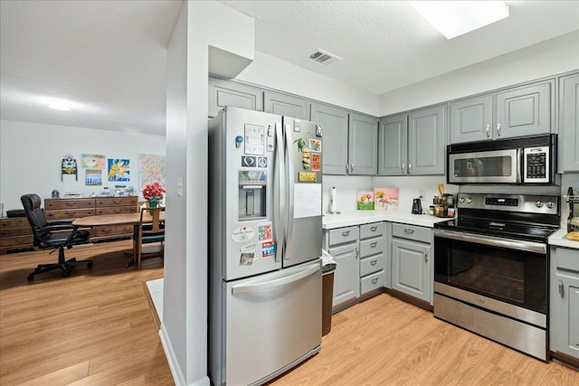 kitchen featuring stainless steel appliances, a textured ceiling, light wood-type flooring, and gray cabinetry