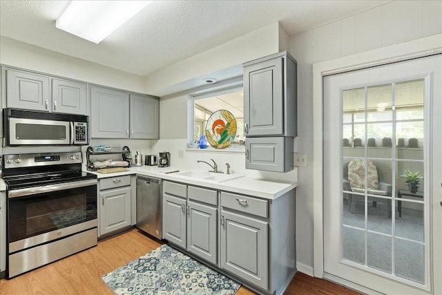 kitchen featuring gray cabinets, stainless steel appliances, sink, and light wood-type flooring