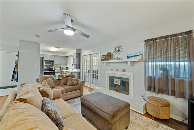 living room featuring a brick fireplace, light wood-type flooring, and ceiling fan