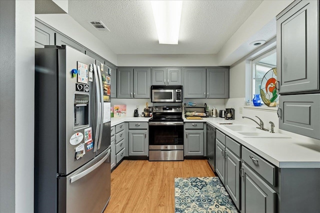 kitchen featuring a textured ceiling, gray cabinetry, light hardwood / wood-style flooring, and appliances with stainless steel finishes