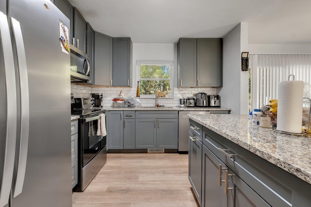 kitchen featuring light wood-style floors, stainless steel appliances, decorative backsplash, and gray cabinetry