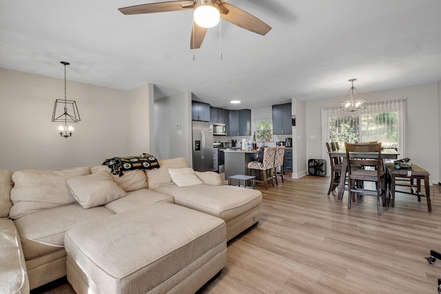 living room featuring ceiling fan with notable chandelier, light wood-type flooring, and baseboards