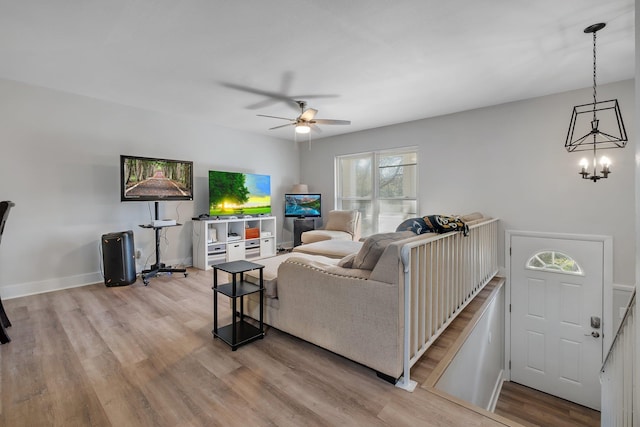 living area with baseboards, wood finished floors, and ceiling fan with notable chandelier