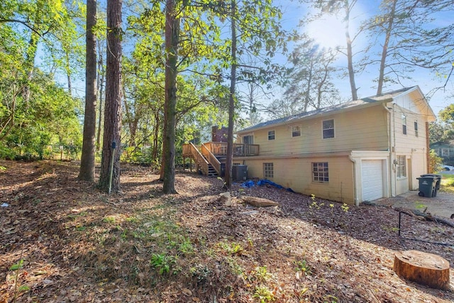 rear view of house with an attached garage, a wooden deck, and stairs