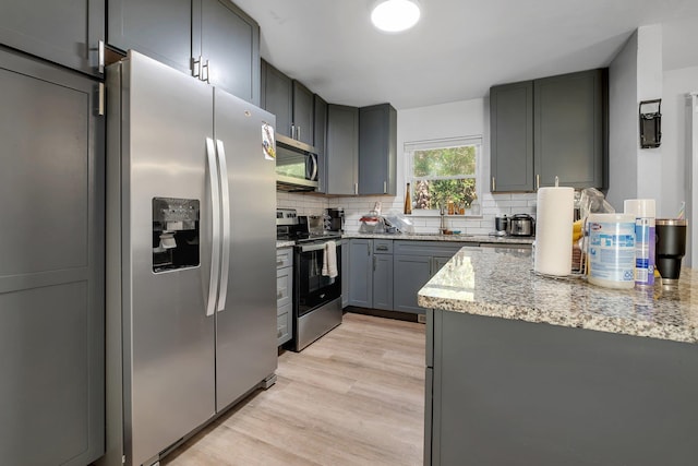 kitchen with light wood-type flooring, appliances with stainless steel finishes, gray cabinets, and decorative backsplash