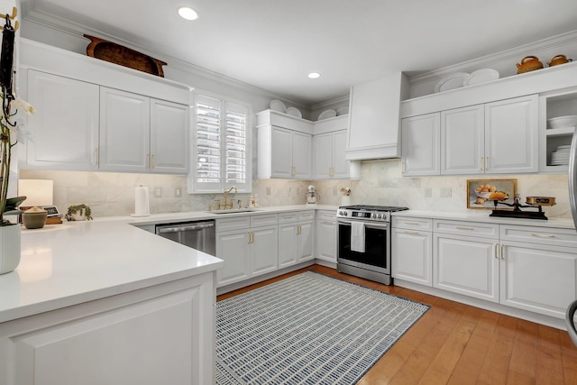 kitchen with sink, stainless steel appliances, light hardwood / wood-style floors, white cabinets, and custom exhaust hood