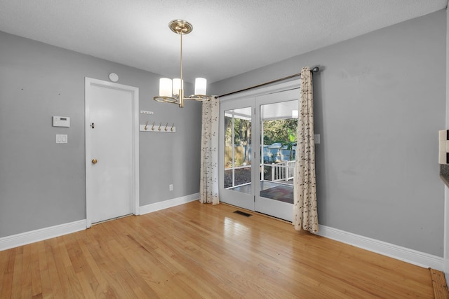 unfurnished dining area with wood-type flooring, a textured ceiling, and a chandelier