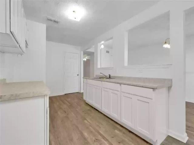 kitchen with light hardwood / wood-style flooring, white cabinets, decorative light fixtures, and sink