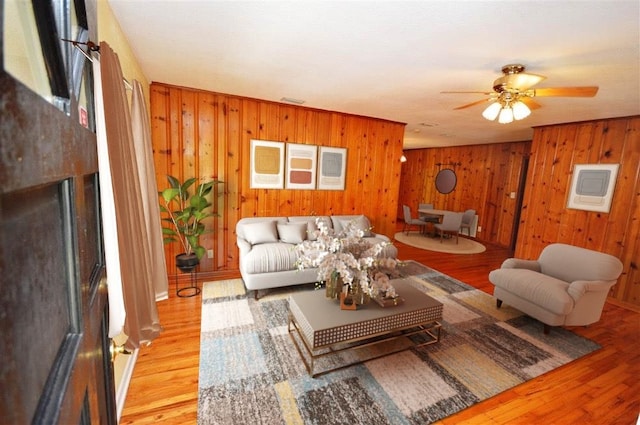 living room featuring ceiling fan, light hardwood / wood-style flooring, and wooden walls