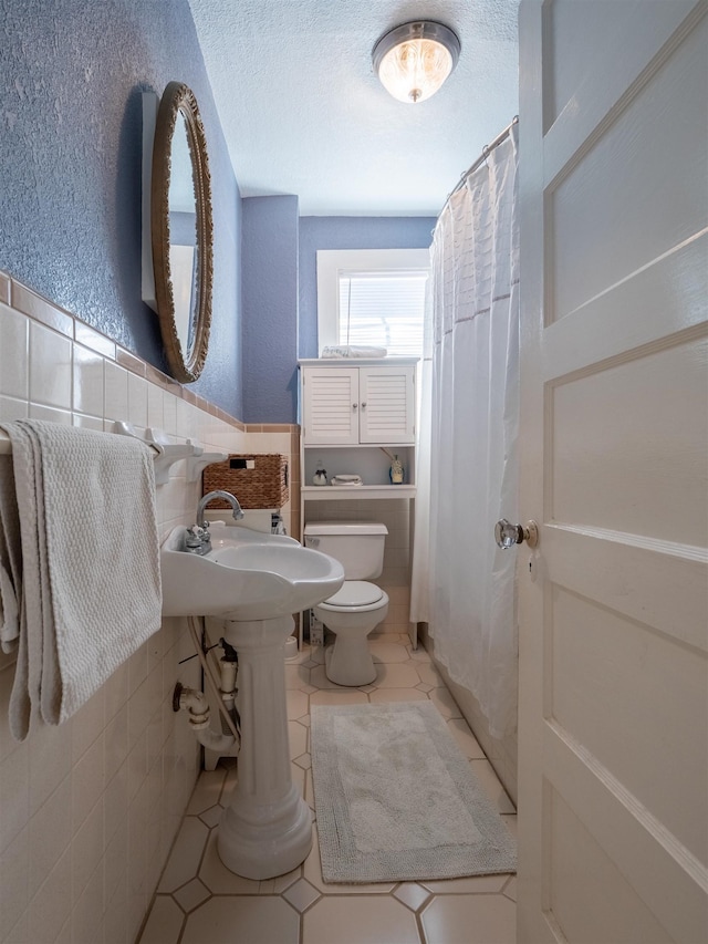 bathroom featuring toilet, tile patterned flooring, tile walls, and a textured ceiling