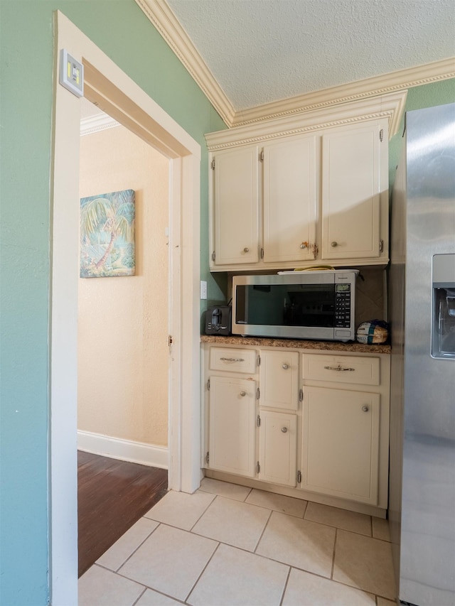 kitchen with a textured ceiling, cream cabinets, crown molding, appliances with stainless steel finishes, and light tile patterned flooring