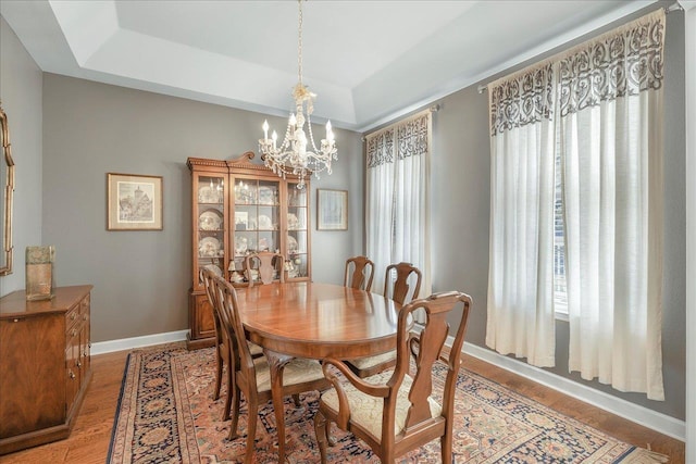 dining space with hardwood / wood-style floors, a chandelier, and a tray ceiling