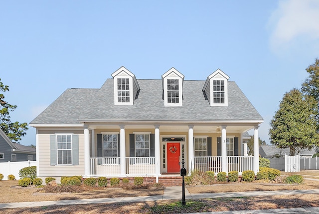 cape cod-style house featuring a shingled roof, fence, and covered porch