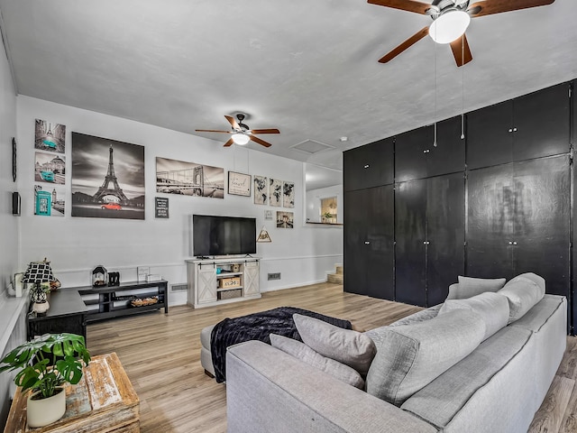 living room with attic access, baseboards, light wood finished floors, and ceiling fan