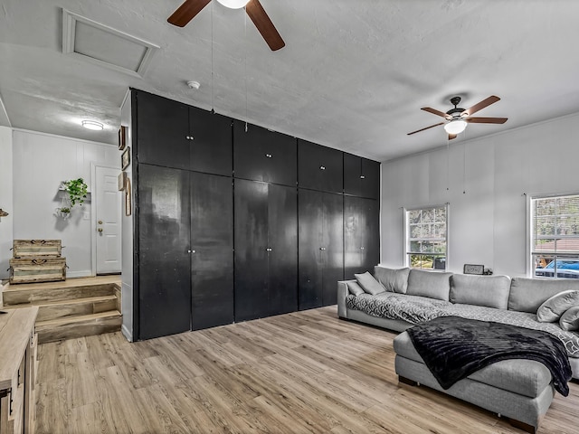 living area with attic access, light wood-type flooring, and a ceiling fan