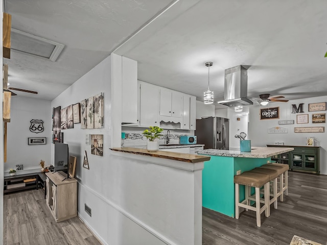 kitchen featuring dark wood-type flooring, ceiling fan, stainless steel fridge with ice dispenser, island exhaust hood, and white cabinetry