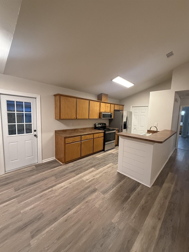 kitchen with lofted ceiling, sink, stainless steel appliances, kitchen peninsula, and hardwood / wood-style flooring