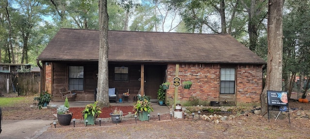 view of front facade with a porch, brick siding, and fence