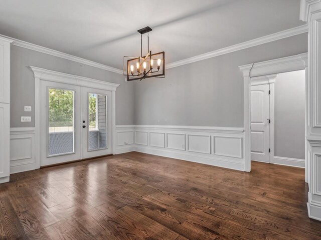 unfurnished dining area with crown molding, an inviting chandelier, wainscoting, french doors, and dark wood-type flooring