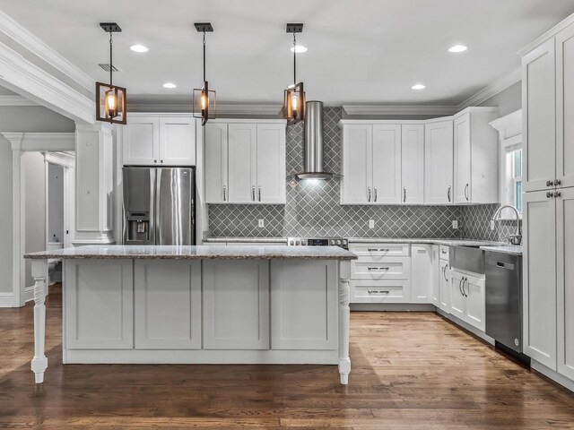 kitchen featuring wall chimney range hood, crown molding, a sink, stainless steel appliances, and a kitchen island