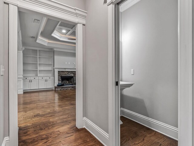 hallway with built in features, baseboards, dark wood-type flooring, visible vents, and ornamental molding