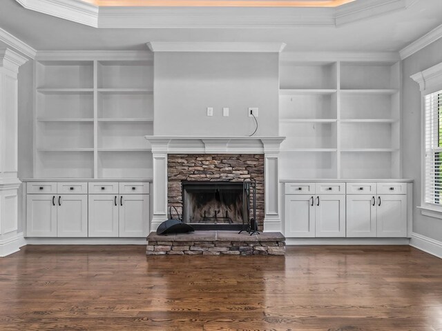 unfurnished living room with a stone fireplace, built in features, ornamental molding, and dark wood-type flooring