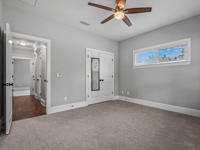 unfurnished bedroom featuring carpet floors, a ceiling fan, baseboards, visible vents, and ornamental molding