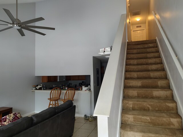 stairs featuring a towering ceiling, tile patterned flooring, and ceiling fan