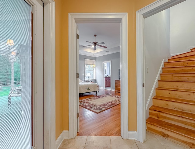 hallway with crown molding, baseboards, stairway, a tray ceiling, and light tile patterned floors