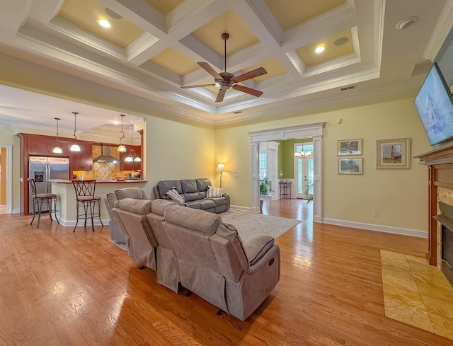 living room with a ceiling fan, a fireplace with flush hearth, ornamental molding, and light wood finished floors