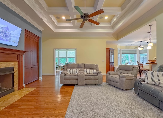 living area featuring light wood finished floors, a tiled fireplace, a ceiling fan, a towering ceiling, and ornamental molding