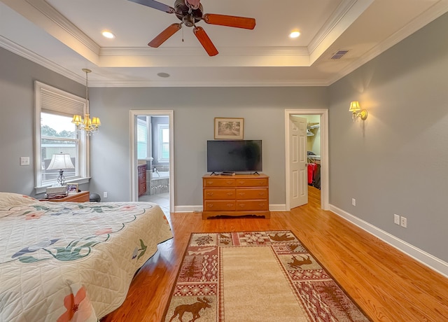 bedroom featuring a walk in closet, a tray ceiling, visible vents, and light wood-style flooring