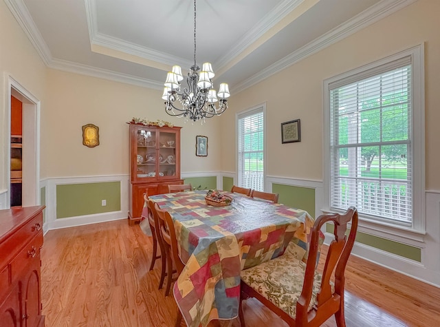dining space with a tray ceiling, a notable chandelier, ornamental molding, and light wood finished floors