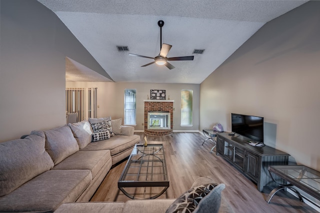 living room featuring a textured ceiling, light hardwood / wood-style floors, ceiling fan, vaulted ceiling, and a brick fireplace