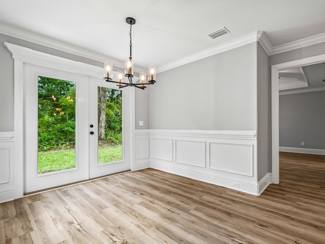 unfurnished dining area with a healthy amount of sunlight, hardwood / wood-style floors, ornamental molding, and an inviting chandelier