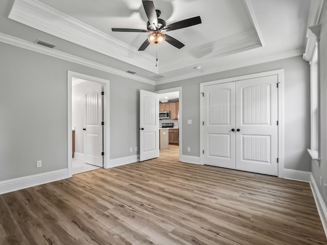 unfurnished bedroom with a tray ceiling, ceiling fan, crown molding, light hardwood / wood-style floors, and a closet